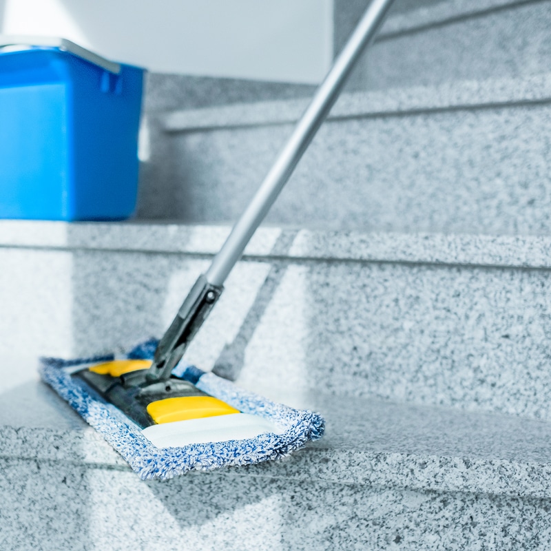 Nettoyage escalier granit : serpillière professionnelle Serpillière plate bleue sur des marches d'escalier en granit gris, avec un seau bleu en arrière-plan. Nettoyage et entretien des sols.