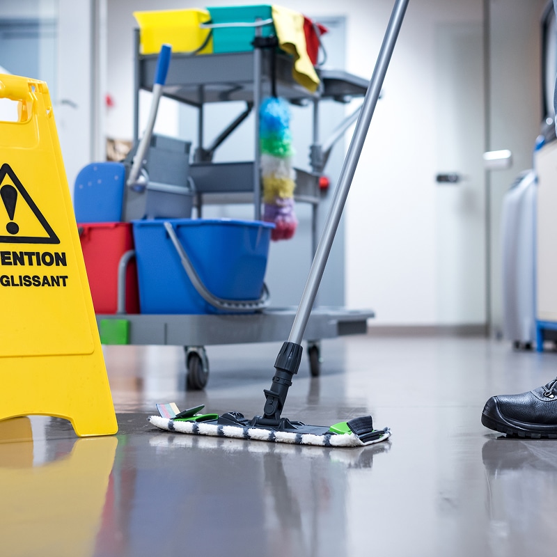 Sol glissant avec serpillière et panneau "ATTENTION GLISSANT" près d'un chariot de nettoyage. Entretien professionnel.